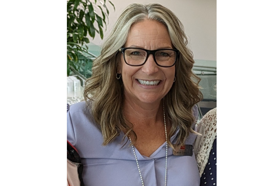 A blonde woman wearing a light blue top is seen smiling